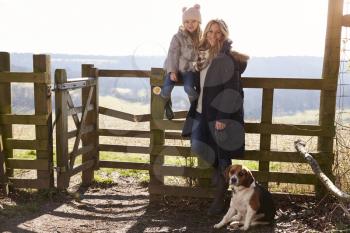 Mother and daughter by a gate in countryside with pet dog
