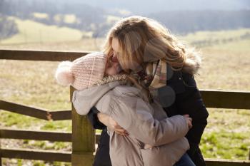 Mother kissing her daughter by a gate in the countryside