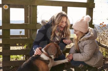 Mother and daughter play with dog in countryside, close up