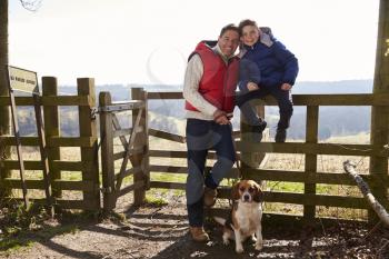 Father stands with dog, son sitting on a rural fence