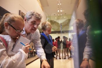 Teacher And Pupils Looking At Artifacts On Display In Museum