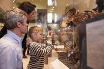 Family Looking At Artifacts In Glass Case On Trip To Museum