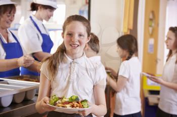 Caucasian schoolgirl holds plate of food in school cafeteria