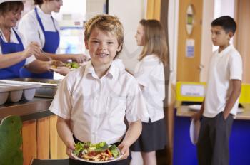 Blonde haired boy holding plate of food in school cafeteria
