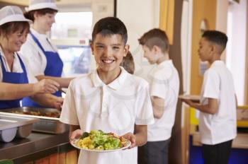 Hispanic schoolboy holds a plate of food in school cafeteria