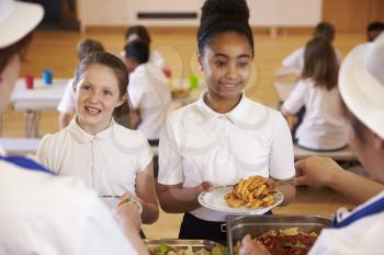 Over shoulder view of girls being served in school cafeteria