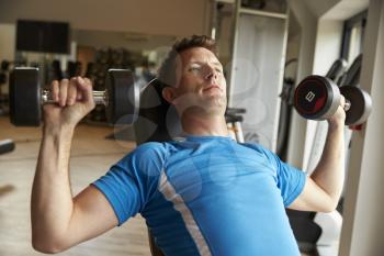 Man works out with dumbbells on a bench at a gym, front view