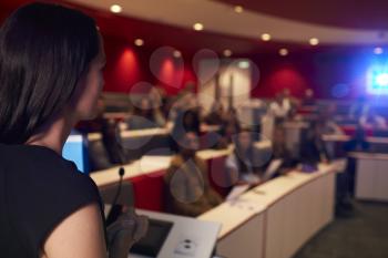 Woman lecturing students in lecture theatre, focus foreground