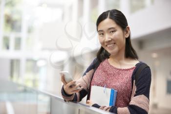 Asian female adult student using phone looks to camera