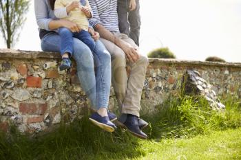 Family Sitting On Wall During Walk In Summer Countryside