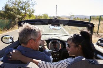 Couple driving in open top car look at each other, back view