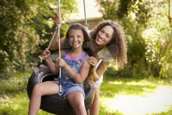 Mother Pushing Daughter On Tire Swing In Garden