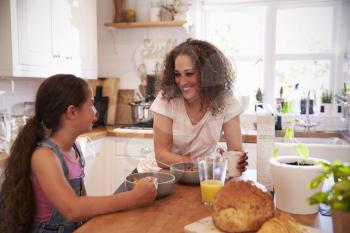 Mother And Daughter Eating Breakfast In Kitchen Together