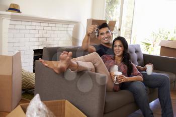 Couple On Sofa Holding Keys Taking A Break On Moving Day