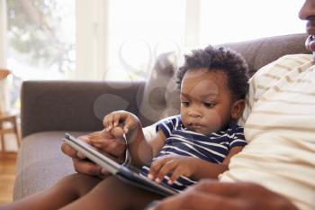 Father And Son Sitting On Sofa At Home Using Digital Tablet
