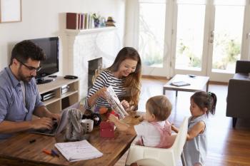 Father Uses Laptop Whilst Mother Plays With Children At Home