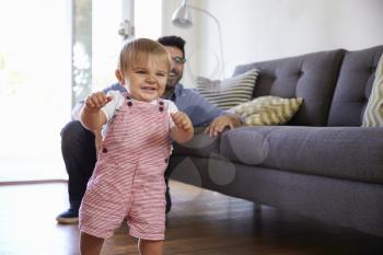 Father Watching Baby Daughter Take First Steps At Home