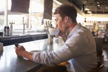 Man Checking Messages On Phone In Coffee Shop