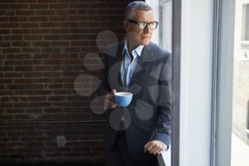 Mature Businessman Standing By Office Window With Coffee