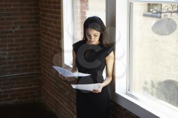 Businesswoman Reading Document Standing By Office Window
