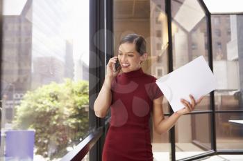 Young white businesswoman on phone looking out office window