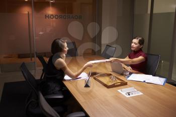 Two businesswomen working late in office passing documents
