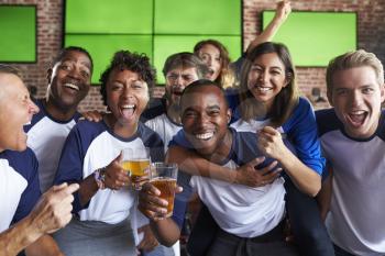 Portrait Of Friends Watching Game In Sports Bar On Screens