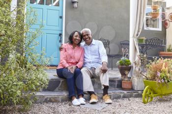Senior couple sit on steps outside their house, full length