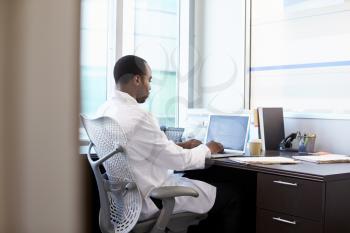 Doctor Wearing White Coat Working On Laptop In Office