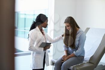 Doctor Talking To Unhappy Teenage Patient In Exam Room