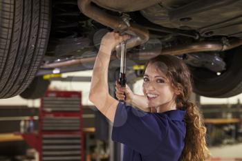 Portrait Of Female Auto Mechanic Working Underneath Car