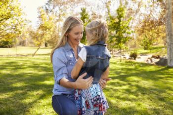 Mother and daughter embracing in park, three quarter length