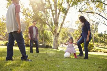Young mixed race family playing with ball in a park, crop