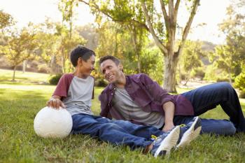Father and son relaxing with soccer ball in a park, close up