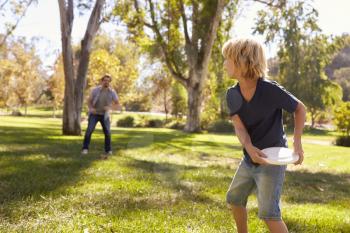Father And Son Throwing Frisbee In Park Together