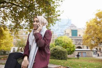 British Muslim Woman On Break Using Mobile Phone In Park