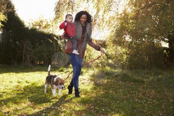 Mother With Child Taking Dog For Walk In Autumn Garden