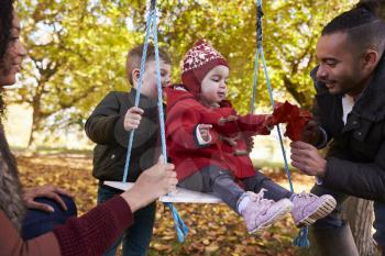 Parents With Children Playing On Tree Swing In Autumn Garden