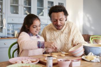 Father And Daughter Decorating Cookies At Home Together