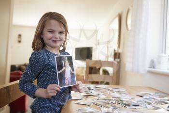 Young Girl Looking At Family Photographs On Table At Home