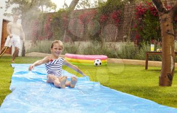 Father And Daughter Having Fun On Water Slide In Garden