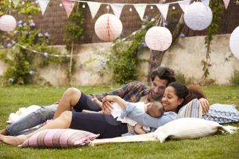 Family With Baby Relaxing On Rug In Garden Together