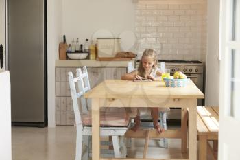 Young Girl At Home Using Digital Tablet On Kitchen Table