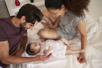 Parents Playing With Baby Daughter In Bedroom At Home