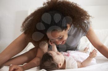 Mother Playing With Baby Daughter In Bedroom At Home
