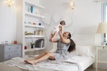 Mother Playing With Baby Daughter In Bedroom At Home