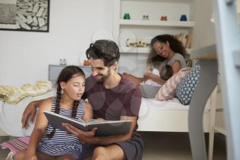 Family With Baby Sitting In Bedroom Reading Book