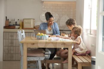 Children Paint At Kitchen Table As Mother Works At Laptop