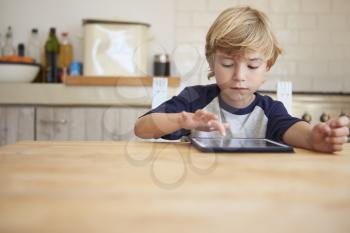 Young boy using tablet computer at kitchen table, front view