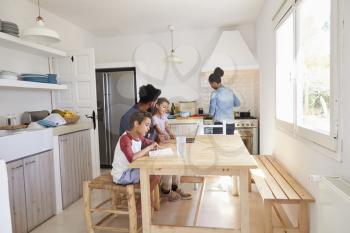 Dad sitting with kids at kitchen table while mum cooks